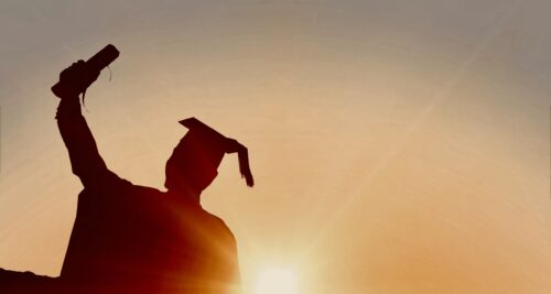 Student holds up diploma as sun sets in front of him
